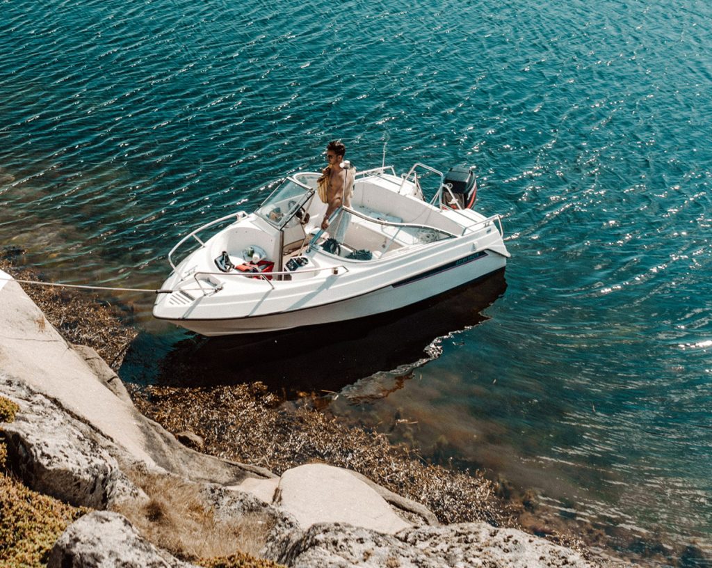 Motorbåt som ligger förtöjd vid en liten ö i svenska skärgården. En man med en picnic-bag på väg ut ur båten.