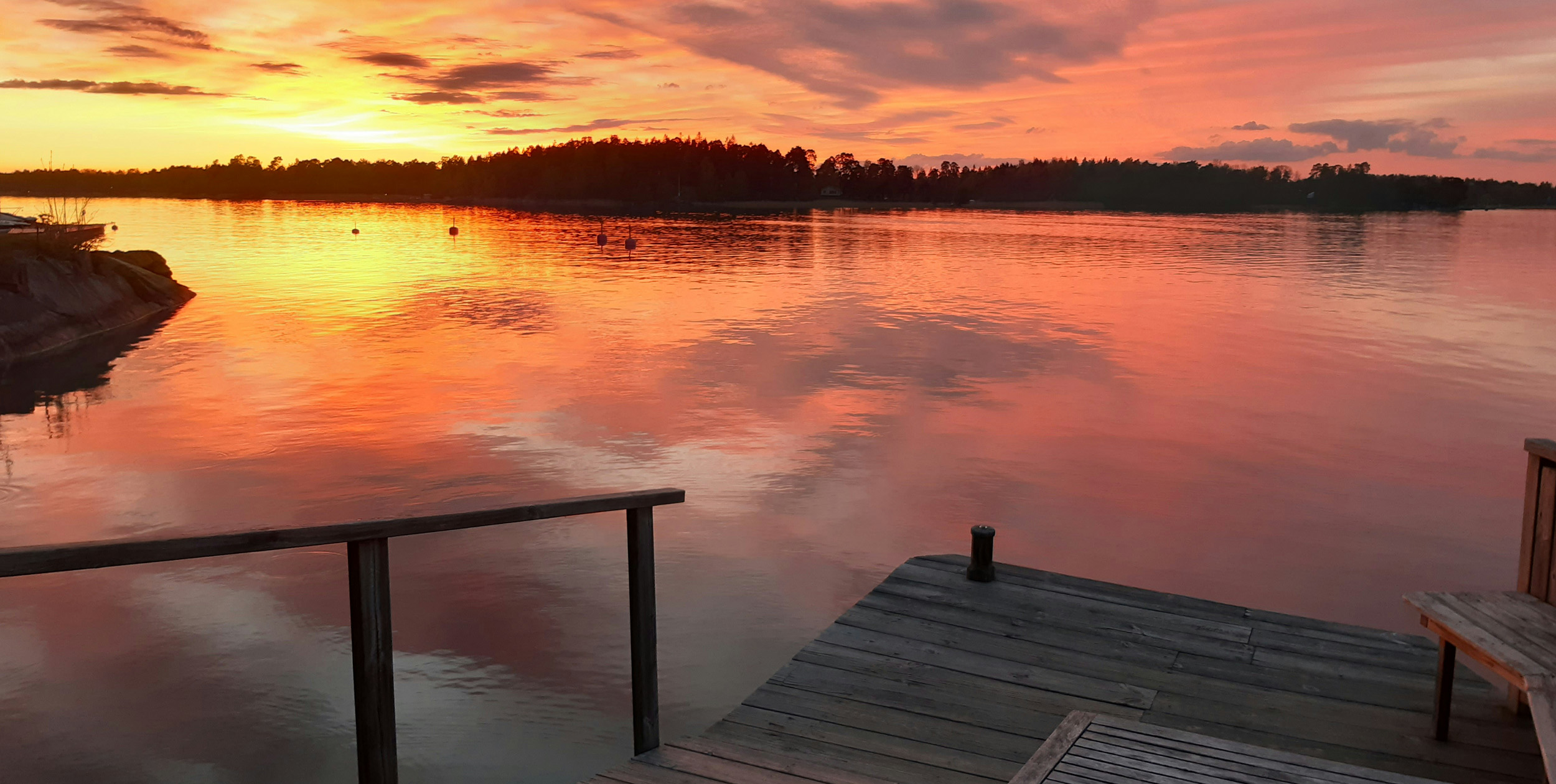 Den svenska skärgåden med ett tidigt morgonljus. Det är den gyllene timmen. Solen, som är på väg upp, och himlen reflekteras mot ett spegelblankt vatten. I förgrunden syns en tom brygga.